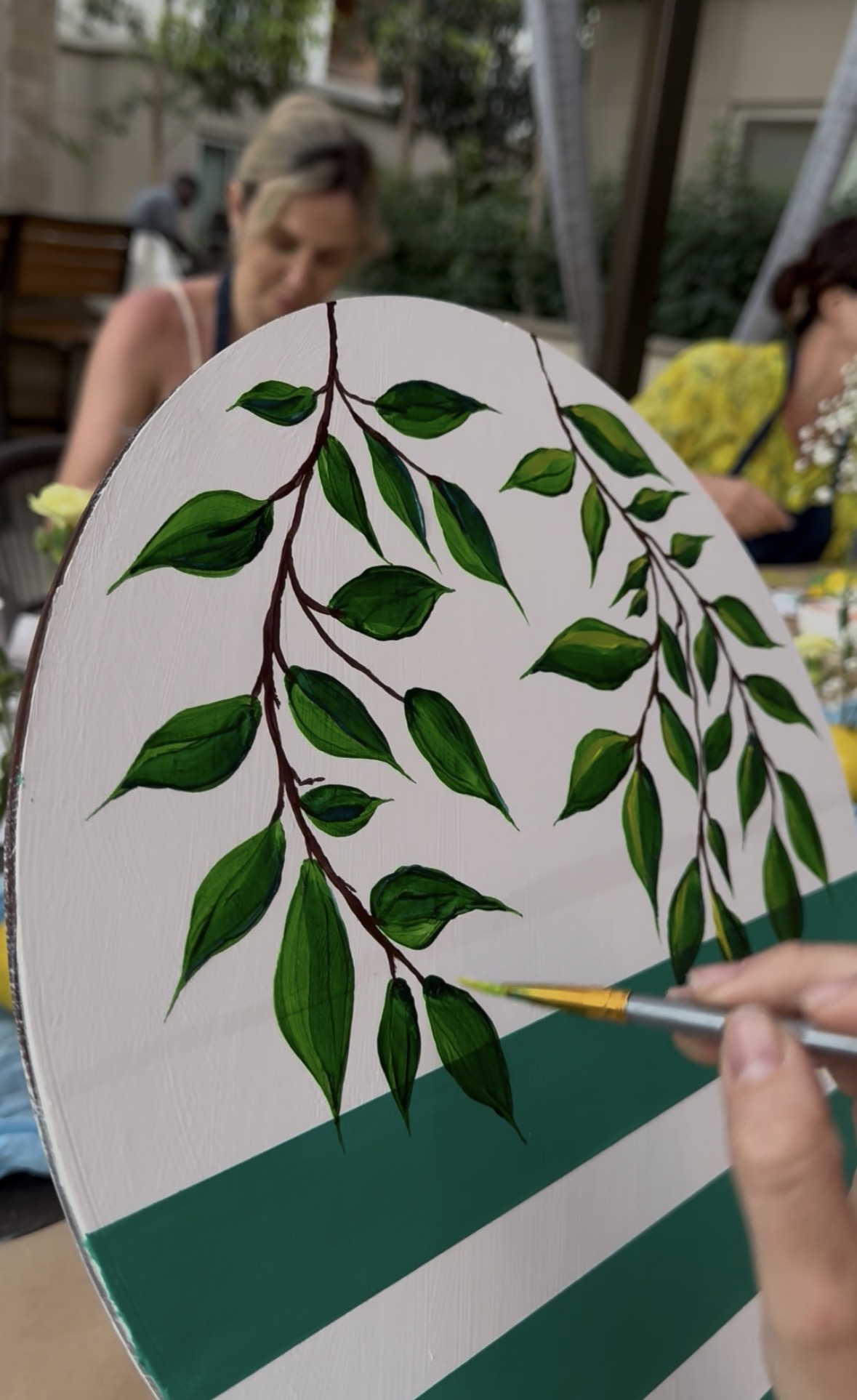 Guest painting green leaves on a striped board