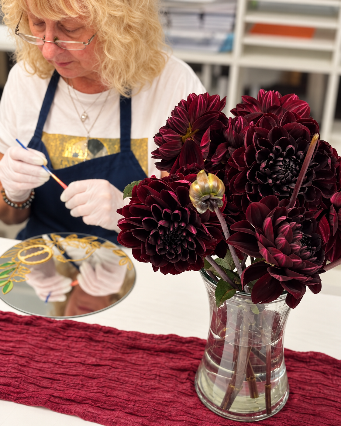 Workshop participant painting beside a vase of burgundy dahlias